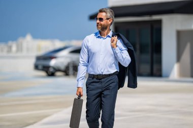 Takım elbiseli İspanyol iş adamı. İş başarısı. Başarılı bir iş adamı yürüyor. Başarılı bir iş adamı park yerinde evrak çantasıyla yürüyor. İş adamı evrak çantasını tutar. Kendine güvenen lider.