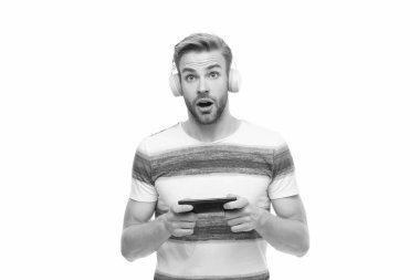 Adam oyun oynamak için akıllı telefon kullanıyor ve beyazla izole edilmiş müzik kulaklıklarıyla online oyun oynuyor..