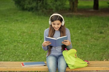 Okuldaki şaşkın kız kitap okuyor ve açık havada sesli müzik dinliyor. Okula dönelim. Eğitim ve bilgi. Kızım sesli kitap dinle ve kitap oku. Audiobook kitaba karşı. Öğrenci kız. Okul eğitimi.