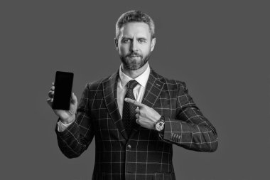 Takım elbiseli adam. Yeni telefon uygulaması. Ürünü sunuyorum. İş uygulamasının reklamı. İspanyol iş adamı telefon ekranını sunuyor. Griler 'de izole edilmiş bir telefon gösteren bir iş adamı. Bunu dene..