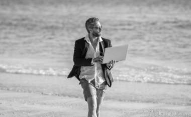 Serbest konsept ve yaz seyahati. İş adamı yaz tatili. Uzaktan kumandalı takım elbiseli iş adamı dizüstü bilgisayarla çalışıyor. Hafta sonu ve iş adamının uzaktan bağımsız çalışması. Uzak bir yaz çalışması. Teselli bul.