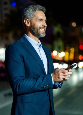 Akıllı telefon kullanan mutlu bir iş adamı. Başarılı bir iş adamı internette sohbet ediyor. Gece vakti yürüyen iş adamı. Dışarıdaki telefonda iş adamı sohbeti. Gece sokakta iş adamı telefonda konuşuyor..