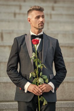 Aşk randevu konsepti. Aşk gülü giymiş yetişkin bir smokin adam. Aşk günü için çiçek hediyesi..