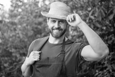 Bahçıvan önlüklü mutlu bahçıvan şapkası takıyor ve açık havada gülümsüyor..