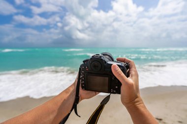 Yazın seyahat. Sahildeki fotoğraf makinesi. Yaz tatili. Seyahat ve fotoğrafçılık. Fotoğrafçı elinde kamerayla fotoğraf çekiyor. Yaz plajında kameralı bir gezgin. Seyahat fotoğrafçılık.