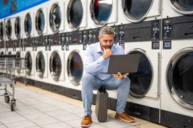 Çamaşır ve teslim tarihleriyle uğraşan yorgun bir işçi. Yoğun iş adamları için aşırı çamaşır yüklemesi. Çamaşırhanede dizüstü bilgisayarla uğraşan meşgul bir adam. Çamaşır ve iş yükleme işinde çok çalışan var. İş-yaşam dengesi.