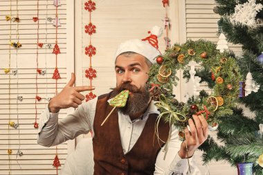 Noel adamı şeker yer. Noel 'de sakallı adam. Yeni yıl tatili. Bıyıklı adam Xmas çelengini tutuyor. İşaret parmağı. - Mutlu yıllar. Noel çelengi süslemesi. Ev için Xmas dekorasyonu.