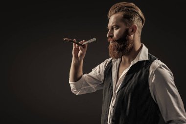 Siyah sakallı hippi berber. Berberdeki kuaförden sakal kesimi. Saç keserken retro bıçak kullanan yakışıklı berber. Modern berber saç kesimi. Boşluğu kopyala.