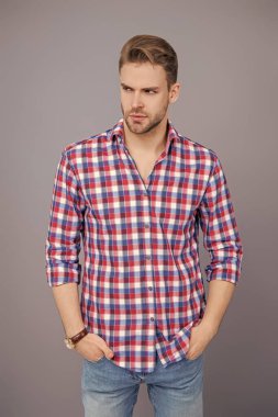 Yakışıklı genç adam. Sıradan gömlekli bir adamın portresi. Gri üzerinde kollarını çapraz tutuyor. Tıraşsız erkek derisi. Erkek güzelliği ve saç stili. Gündelik giyinen milenyum adamı. Moda eklentisi.