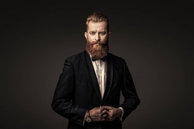 Sakallı damat kendinden emin ve hırslı hissediyor. Smokinli erkek giysili adam Griler 'de izole edilmiş. Smokinli adam resmi erkek giyim bölümünde. Yakışıklı sakallı adam smokin giyer. Şık smokin papyonu. Gerçek zarafet.