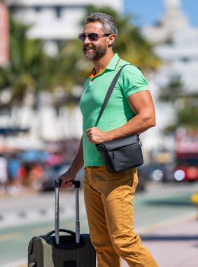 Sokakta yürüyen İspanyol turist. Tropikal şehirde bavullu bir turist. 40 'lı yılların turisti yaz tatilinde. Seyahat bagajı. Yaz turu. Gezgin yaz tatilinin tadını çıkar. Yeni macera.