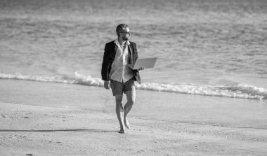 Uzaktan kumandalı takım elbiseli iş adamı dizüstü bilgisayarla çalışıyor. Hafta sonu ve iş adamının uzaktan bağımsız çalışması. Zihnini şarj et. Serbest konsept ve yaz seyahati. İş adamı yaz tatili.