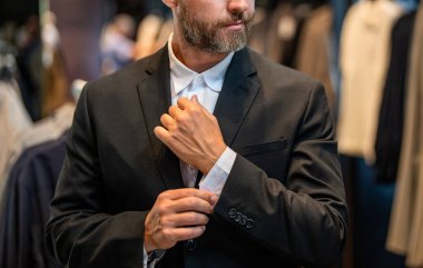 İspanyol iş adamı terzilik ve takım elbise seçiyor. Bespoke terziliği. Takım elbise mağazasında iyi giyimli erkek model. Perakende satış asistanı şık bir adamın takım elbise bulmasına yardımcı olur. İşadamı şık bir takım elbise seçmiş..