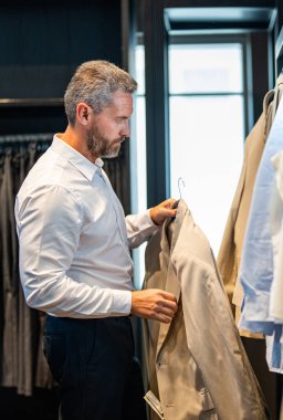 İspanyol iş adamı terzilik ve takım elbise seçiyor. Bespoke terziliği. Takım elbise mağazasında iyi giyimli erkek model. Perakende satış asistanı şık bir adamın takım elbise bulmasına yardımcı olur. İşadamı şık bir takım elbise seçmiş..