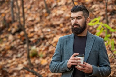 Kahve molası. Günlük stil rutini. Sakallı adam sonbahar şehrinde kahve içiyor. Sonbahar adamı elinde kahve fincanıyla parkta. İş hayatı, mola zamanı. Sabah kahvesi içen adam. Şık giyinmiş..