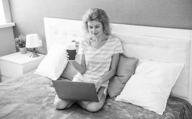 Kadın serbest çalışan ev sohbetinde kahveyi dizüstü bilgisayarında tutuyor. Serbest çalışan bir kadın evde çalışıyor. Serbest çalışan biri için ev işi. Yatakta dizüstü bilgisayarlı bir kadın.