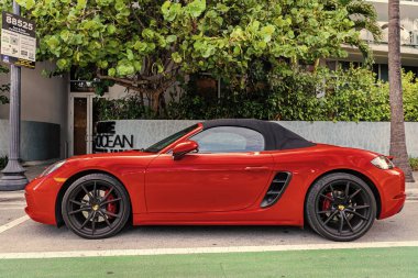 Miami Beach, Florida USA - 9 Haziran 2024: 2018 Porsche 718 Boxter 's orange color at Miami Beach. Ocean 'daki lüks araba porshche' si Miami plajına gidiyor. yan görünüm