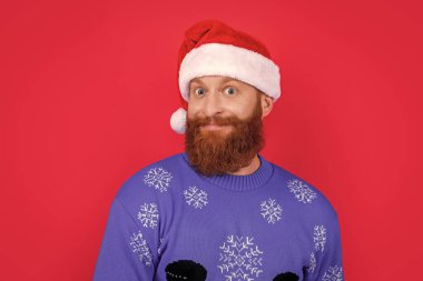 Kafkasyalı mutlu bir adamın portresi Noel süveteri ve kırmızı arka planda izole edilmiş Noel Baba şapkası. Adam Noel 'i kutluyor. Mutlu Noeller..