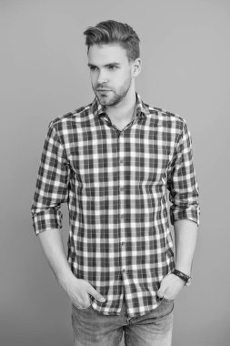 Milenyum erkeğinin gündelik tarzı. Sıradan bir tişörtle genç bir adamın portresi. Tıraşsız adamın şık bir portresi. Gri yolda izole edilmiş bir adam. Kareli gömlek giyen milenyum adamı. Modaya uygun saç modeli..