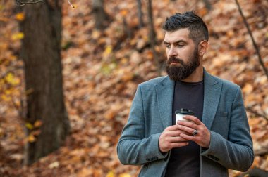 Sabah kahvesi içen adam. Kahve molası. Günlük stil rutini. Sakallı adam sonbahar şehrinde kahve içiyor. Sonbahar adamı elinde kahve fincanıyla parkta. İş hayatı, mola zamanı. Sokak yürüyüşü.