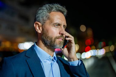 Patrona telefon var. İletişim ve müzakere. Reklam portresi. İş adamı dışarıda telefonla konuşuyor. İş adamı arıyor. İş iletişimi gece şehri. İş görüşmesi çağrısı.