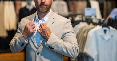 Bespoke terziliği. Perakende asistanı şık bir adamın takım elbise bulmasına yardım ediyor. Takım elbiseli şık bir adam. İşadamı şık bir takım seçmiş. İspanyol iş adamı terzilik takımını seçiyor. Kesik manzaralı. Boşluğu kopyala.