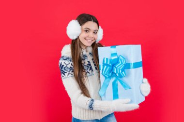 Noel tatili. Kış kulaklıklarıyla Xmas 'lı pozitif bir genç kız. Genç kız Xmas mevcut kırmızı arka planda izole.