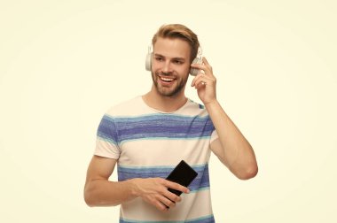 Beyazda izole edilmiş kablosuz kulaklıklı modern telefon. Milenyum adamı kulaklıkla müzik dinliyor. Telefon kullanan kulaklıklı bir adam. Z jenerasyonu elemanı eğitim ya da müzik için telefon uygulaması kullanıyor.