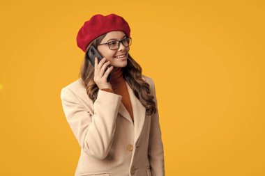 Telefonla arayan bir kız. Ergenlik çağı. Telefonu olan ergen bir kız. İletişim. Sarıda izole edilmiş telefonu kullanan sonbahar kızı. Sonbahar tarzı beresi ve ceketi olan mutlu bir genç kız. Sonbahar biçimi.