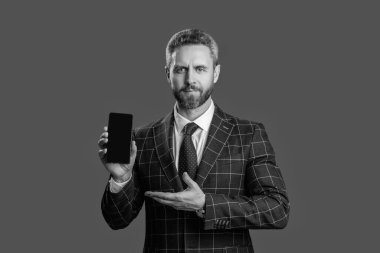 Ürünü sunuyorum. İş uygulamasının reklamı. İspanyol iş adamı telefon ekranını sunuyor. Griler 'de izole edilmiş bir telefon gösteren bir iş adamı. Takım elbiseli adam. Yeni telefon uygulaması.