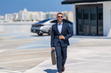 Başarılı bir iş adamı yürüyor. Başarılı bir iş adamı park yerinde evrak çantasıyla yürüyor. İş adamı evrak çantasını tutar. Takım elbiseli İspanyol iş adamı. İş başarısı. Başarılı liderlik..