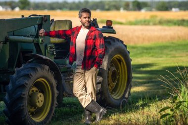 Traktörde olgun bir adam var. Traktör sürücüsü. Tarım ve saha işleri. Çiftçi dışarıdaki traktörde sakız botu giyiyor. Ekin hasadı. Tarım ekipmanları. Hasat makineli çiftçi.