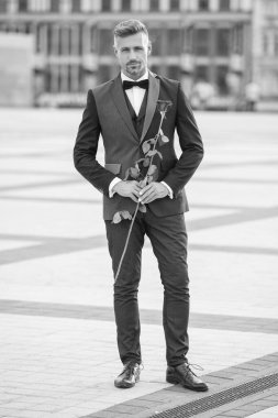 Smokinli zarif bir damat. Damat dışarıda smokin papyon takıyor. Kırmızı güllü yetişkin damat.