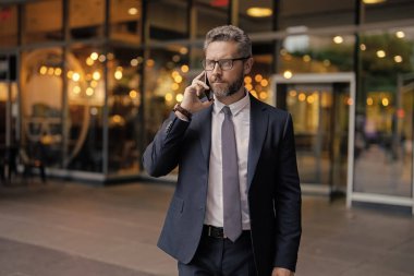 Ciddi İspanyol iş adamlarının telefon görüşmeleri var. İş görüşmesi. Takım elbiseli adam telefonda konuşuyor. Telefon var. Mobil iletişim. İletişim. İş adamı açık havada akıllı telefonda konuşur..