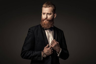 Yakışıklı sakallı adam smokin giyer. Şık smokin papyonu. Sakallı damat kendinden emin ve hırslı hissediyor. Smokinli erkek giysili adam Griler 'de izole edilmiş. Smokinli adam resmi erkek giyim bölümünde. Mükemmel biçim.