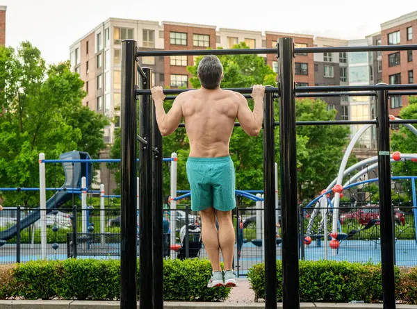 Güçlü bir atlet. Dışarıdaki spor salonunda bir adam var. Güçlü sırt kası olan kaslı bir adam. Spor salonu barı. Spor barfiks egzersizi. Spor eğitimi. Adam barfiks egzersizi yapıyor. Kas kasları ve trisepsler. Eğitim gövdesi.