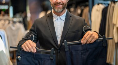 Perakende asistanı şık bir adamın pantolon bulmasına yardım ediyor. Pantolonu olan şık bir adam. İş adamı mağazadan şık pantolonlar seçer. İspanyol adam terzi pantolonu seçiyor. Kesik manzaralı. Takım elbiseli manken..