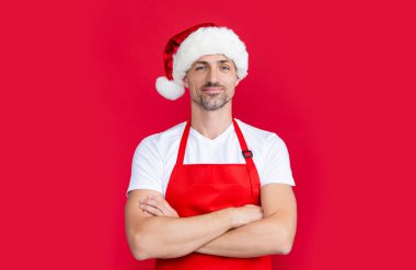 Kırmızı kahve önlüklü ve Noel Baba şapkalı gülümseyen olgun bir adam..