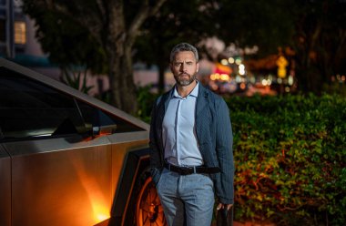 Başarı ve güven. Gece vakti evrak çantasıyla başarılı bir iş adamı. İş adamı evrak çantasını tutar. Lüks arabanın yanında yakışıklı bir iş adamı. İş başarısı. Otoparkta başarılı bir iş adamı..