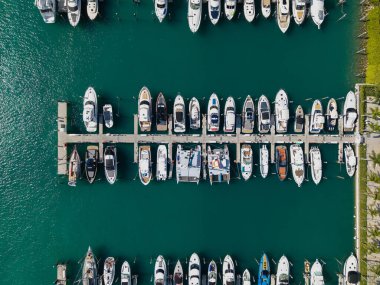 Marinaya yanaşmış lüks yatların havadan görüntüsü. Yatların yukarıdan aşağıya insansız hava aracı görüntüsü. Tekneler ve yelkenliler manzaralı deniz kıyısında. Yat kıyı şeridi boyunca ilerliyor. Şafak vakti liman gemilerle doldu.