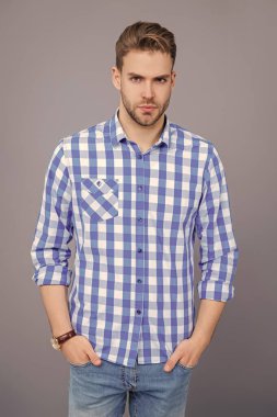 Tıraşsız adamın zarif portresi. Gri yolda izole edilmiş bir adam. Kareli gömlek giyen milenyum adamı. Milenyum erkeğinin gündelik tarzı. Sıradan tişörtlü bir adamın portresi. Erkek giyim.