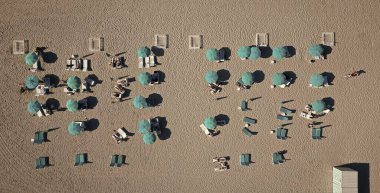 Güneş yatağı ve şemsiyeli kumsal manzarası. Sahilde güneşlenen insanlar. Yaz tatili. Yazın deniz kenarında tatil. Deniz, plaj şemsiyesi altında rahatlar. Denize yolculuk.