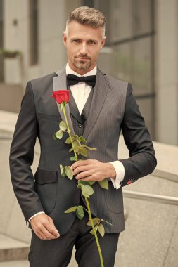 Siyah smokinli zarif adam. Smokin giymiş, papyonlu bir adam. Kırmızı gül tutan yakışıklı smokinli adam..