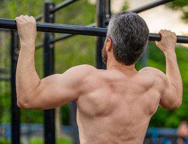 Spor eğitimi. Adam barfiks egzersizi yapıyor. Kas kasları ve trisepsler. Güçlü bir atlet. Dışarıdaki spor salonunda bir adam var. Güçlü sırt kası olan kaslı bir adam. Spor salonu barı. Spor barfiks egzersizi. Vücut ağırlığı.