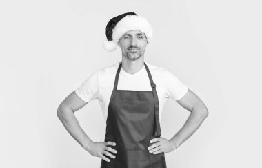 Kırmızı şef önlüğü ve Noel Baba şapkası giymiş neşeli olgun bir adam..