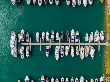 Marinaya yanaşmış lüks yatların havadan görüntüsü. Yatların yukarıdan aşağıya insansız hava aracı görüntüsü. Tekneler ve yelkenliler manzaralı deniz kıyısında. Yat kıyı şeridi boyunca ilerliyor. Şafak vakti liman gemilerle doldu.