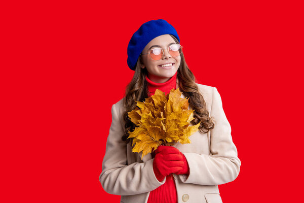 Stylish teen girl isolated on red with maple leaf. Autumn leaf arrangement. Girl with maple leaf wear beret. Fall season beauty. Autumn style. Fallen autumn leaves. September season.
