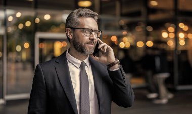 İş görüşmesi. Takım elbiseli adam telefonda konuşuyor. Telefon var. Mobil iletişim. İletişim. Uzayı kopyala İş adamı açık havada akıllı telefondan konuşur. Amerikalı iş adamının telefon konuşması var..