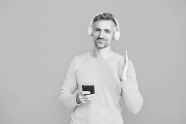 Telefon uygulaması kullanan adam mavi ile izole edilmiş. Telefonla müzik dinlemek. Müzik yaşam tarzı. Ses çalma listesi. Kulaklık takan olgun bir adam. Kulaklıklı adam telefonda spor için çalma listesi seçiyor..