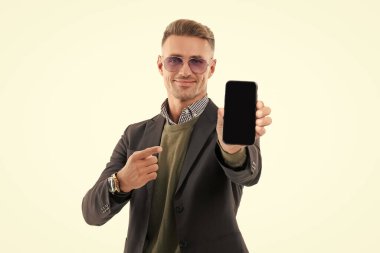 Olgun iş adamı telefon ekranını sunuyor. İşadamı telefonu beyaza çevirerek işaret ediyor. Adam yeni iş telefonu uygulamasını gösteriyor. Ürünü sunuyorum. İş uygulamasının reklamı.